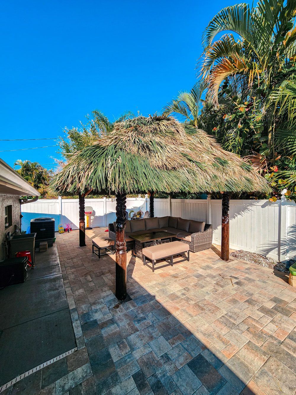 Patio with thatch roof, seating area, and brick patio. Palm trees and blue sky visible.