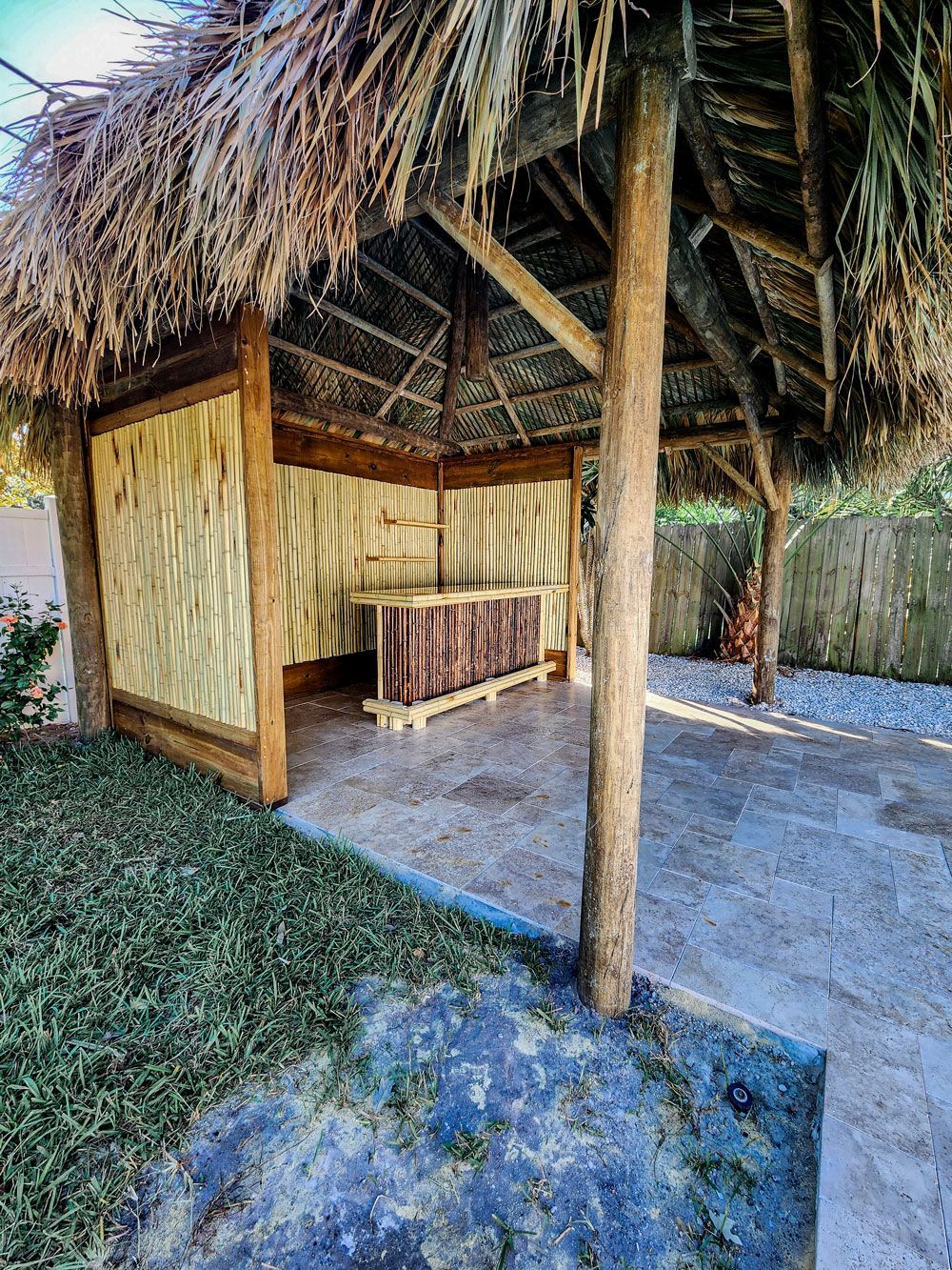 Tiki hut with thatched roof and bamboo walls, built on a paved patio next to green grass.