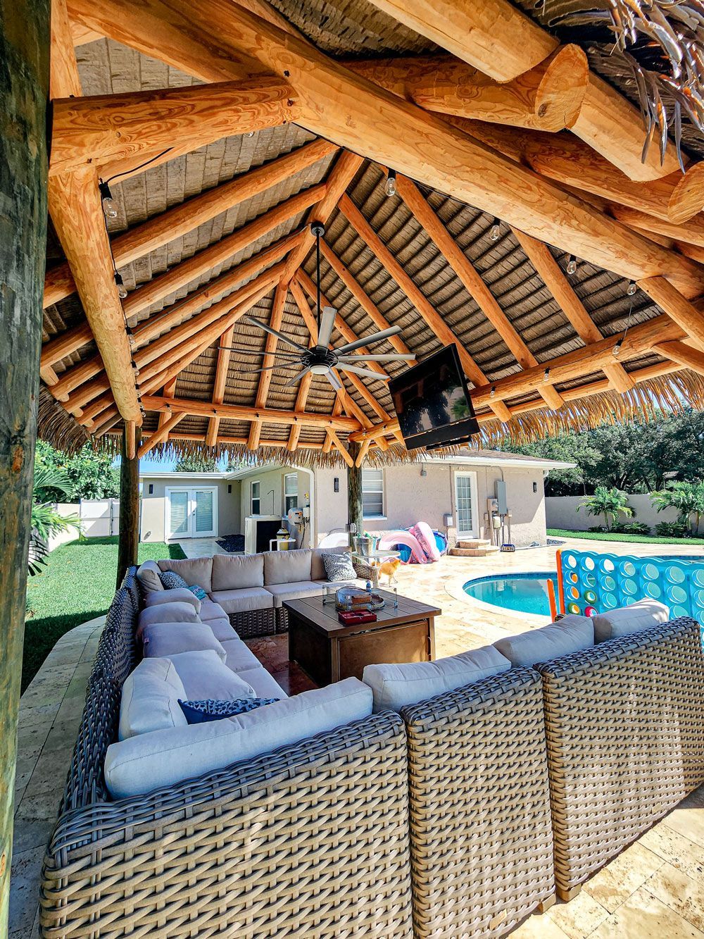 Outdoor lounge with thatched roof, wicker sofa, pool.