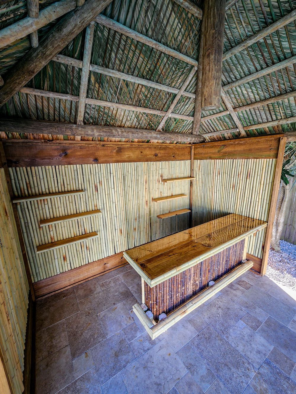 Interior of a rustic bar with bamboo walls, shelves, and counter under a thatched roof.