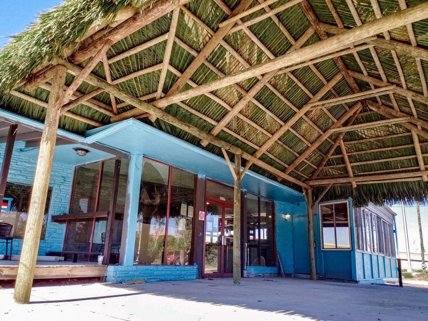 Blue building with a thatched roof, possibly a beachside restaurant or bar, on a sunny day.