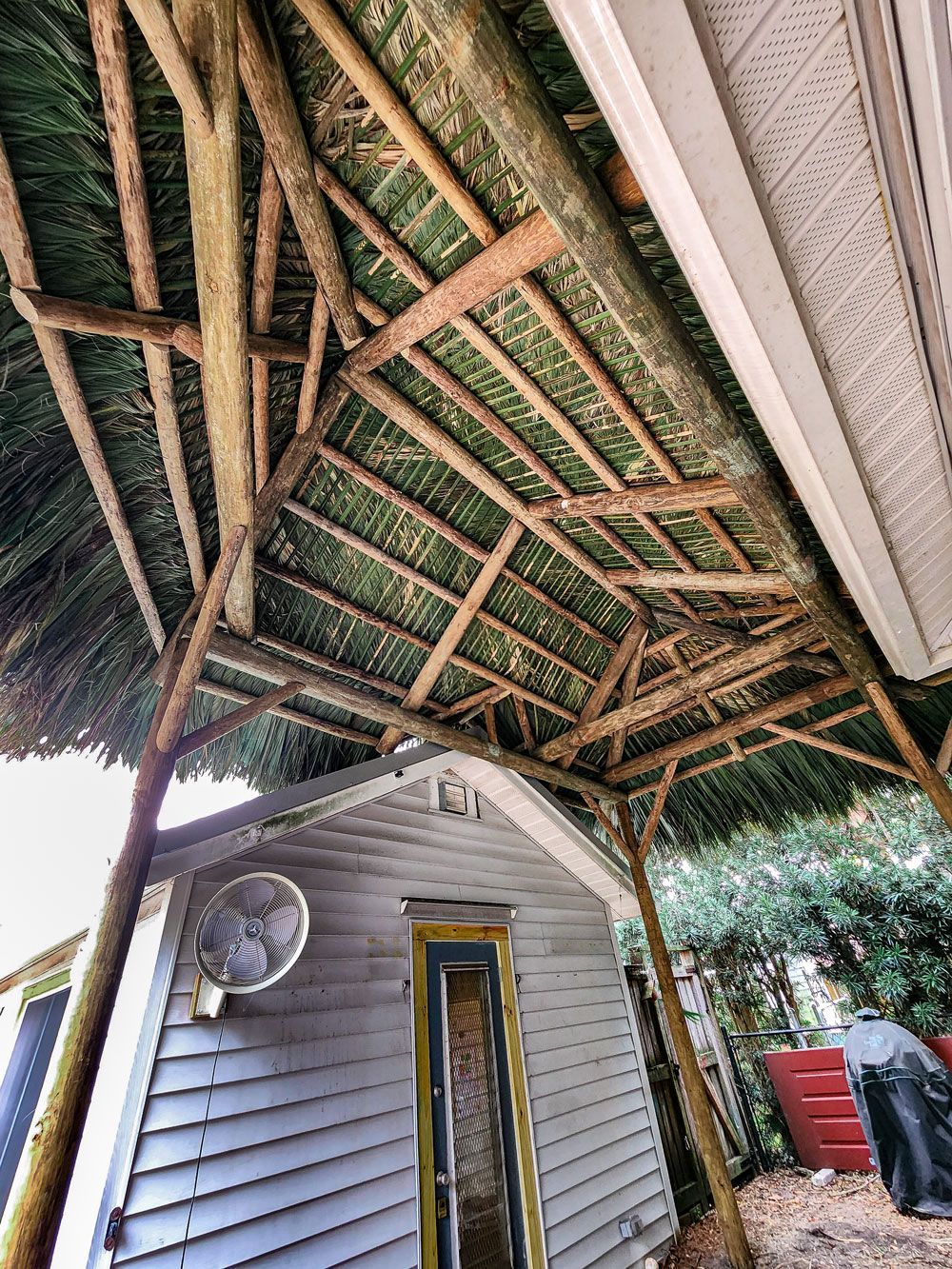 Wooden-framed roof covering a small gray building. Green thatch roof with supporting beams.