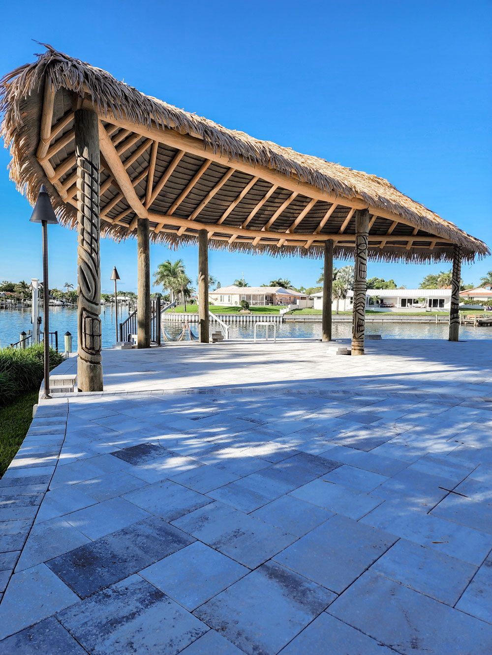 Thatched roof gazebo overlooking water with blue sky and stone patio.