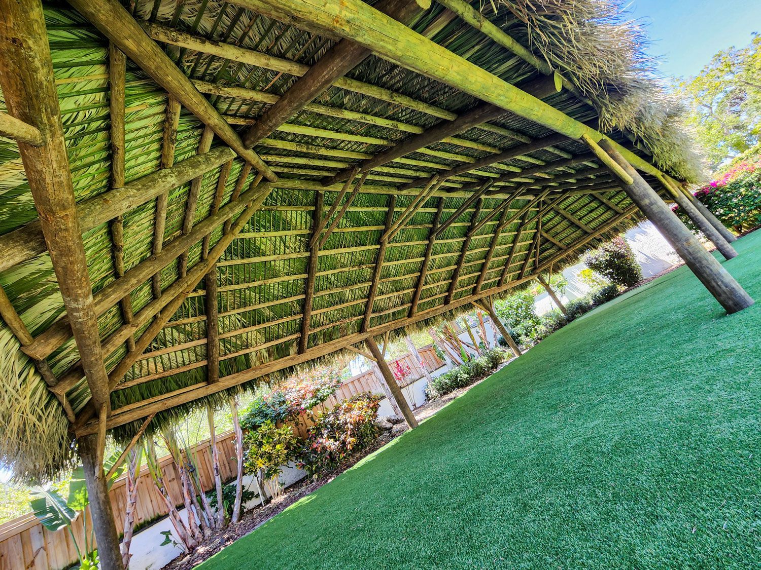 Wooden gazebo with thatched roof over green lawn.