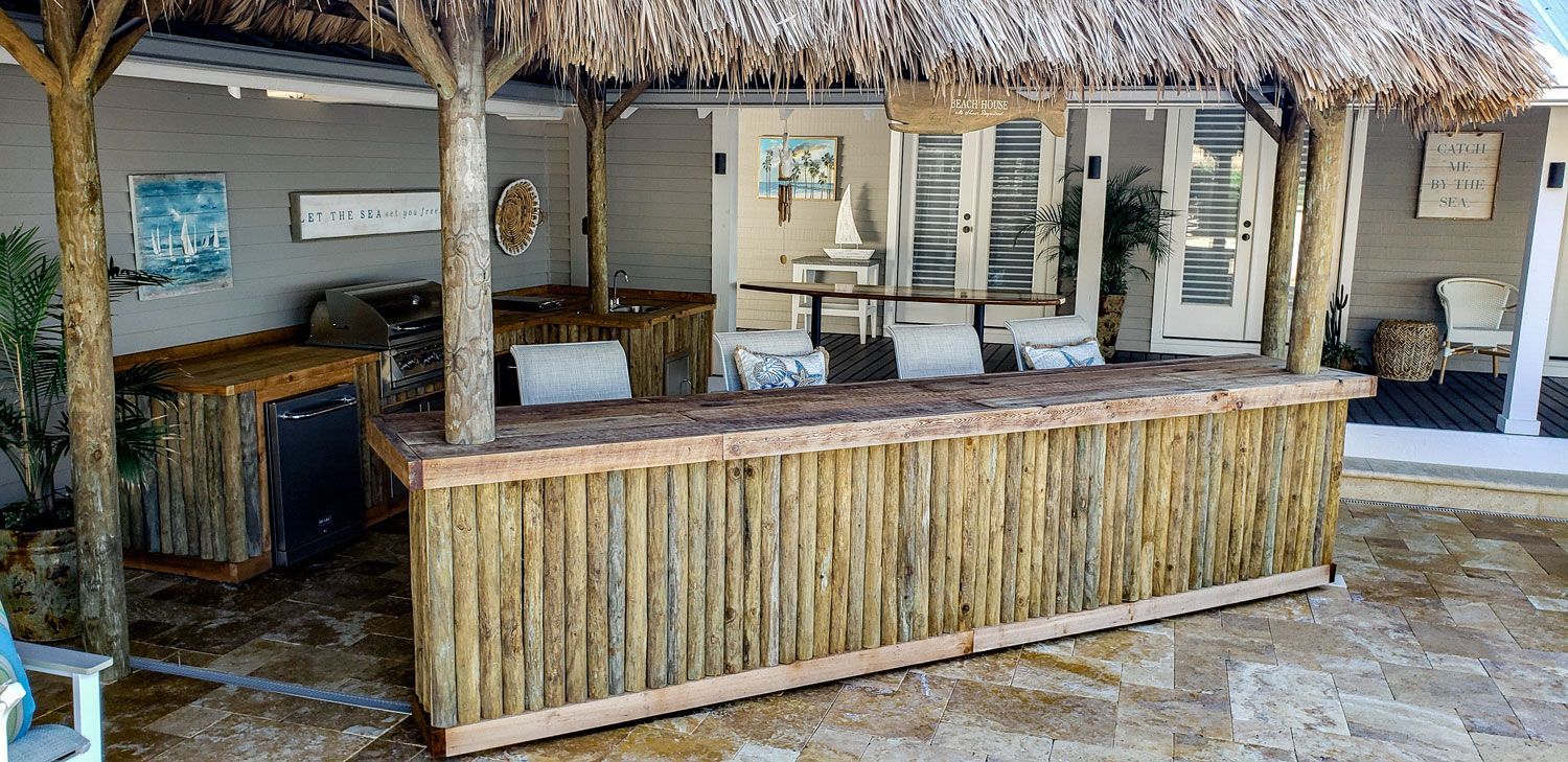 Outdoor tiki bar with thatched roof, wooden counter and bar stools.