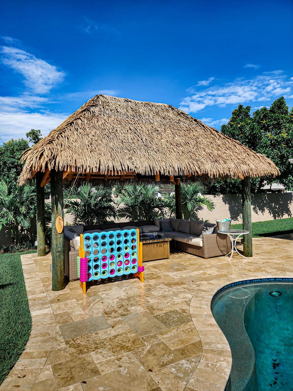 Tiki-style gazebo with a Connect Four game by a pool. Clear blue sky.