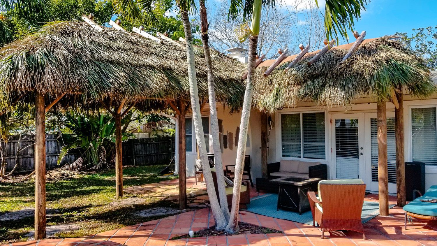 Backyard patio with thatched roof shade structures, red brick, and seating.