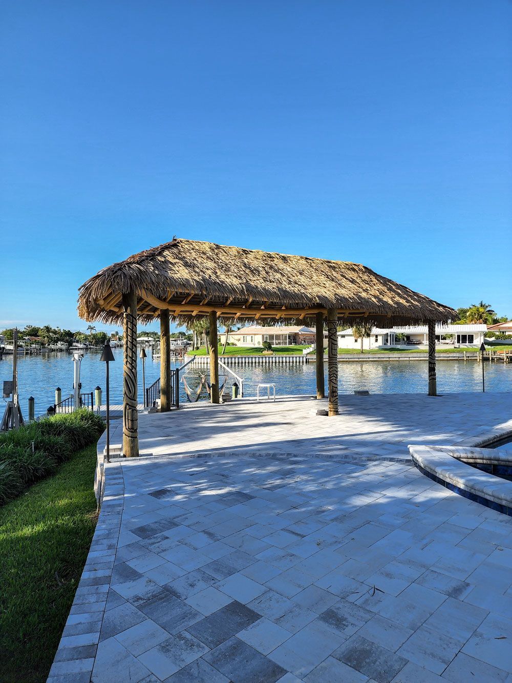 Thatched roof tiki hut on a dock overlooking a canal, under a blue sky.