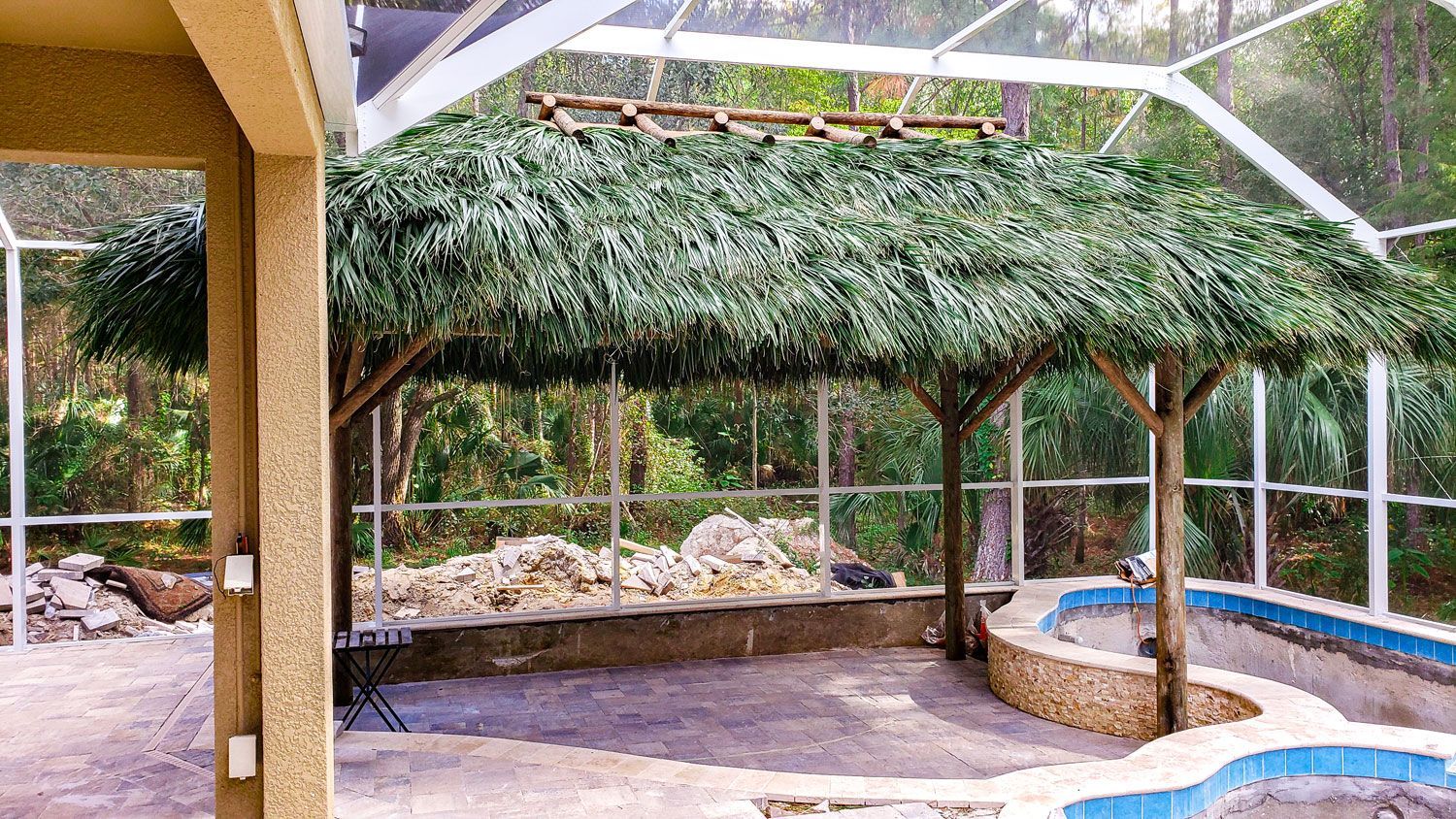A tiki hut with a thatched roof over a patio next to a pool.
