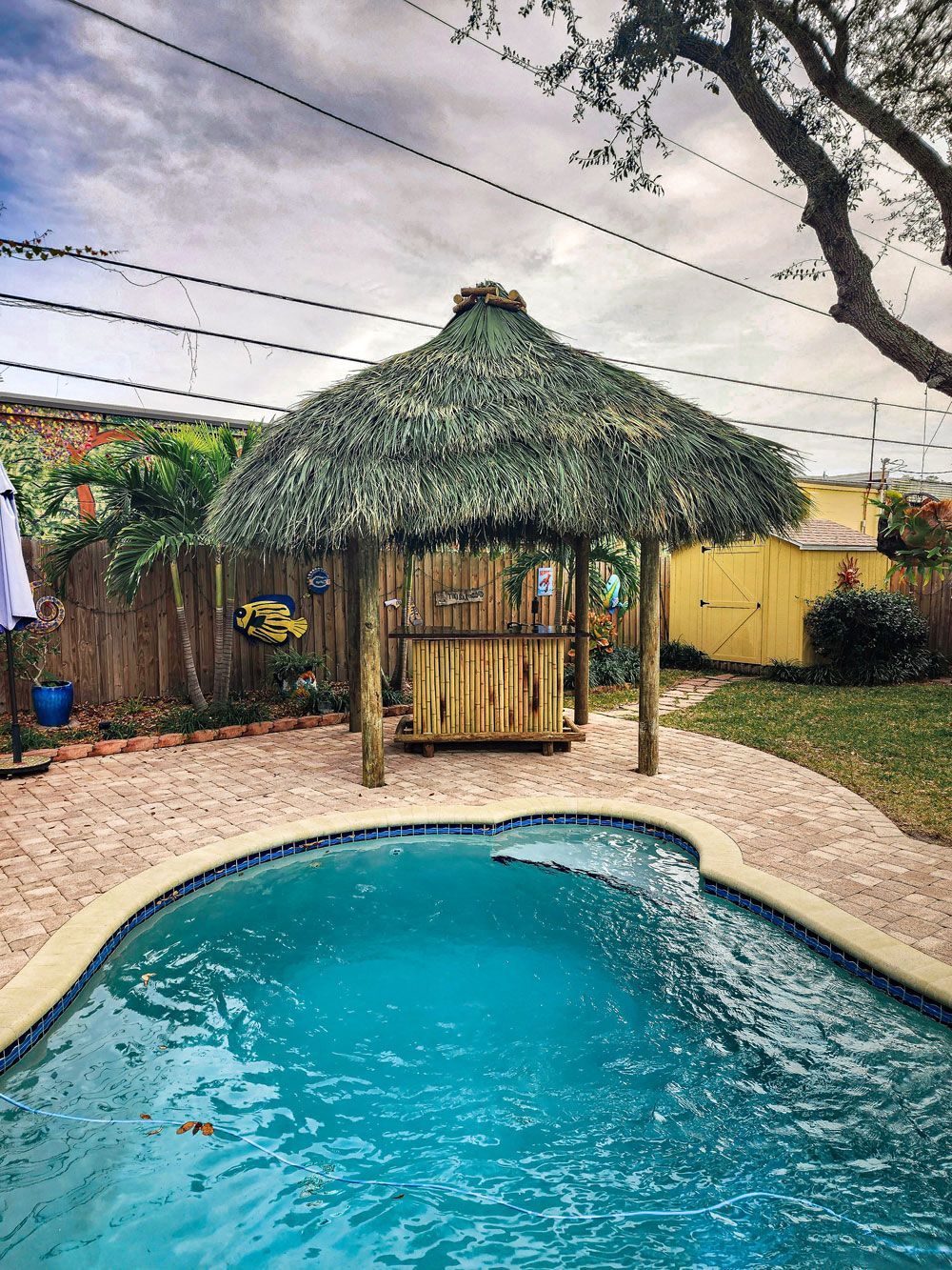 Pool with thatched roof tiki bar in backyard setting.