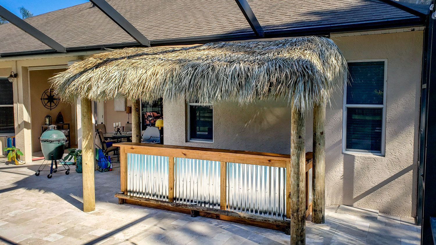 Outdoor tiki bar with corrugated metal and thatched roof on a patio.