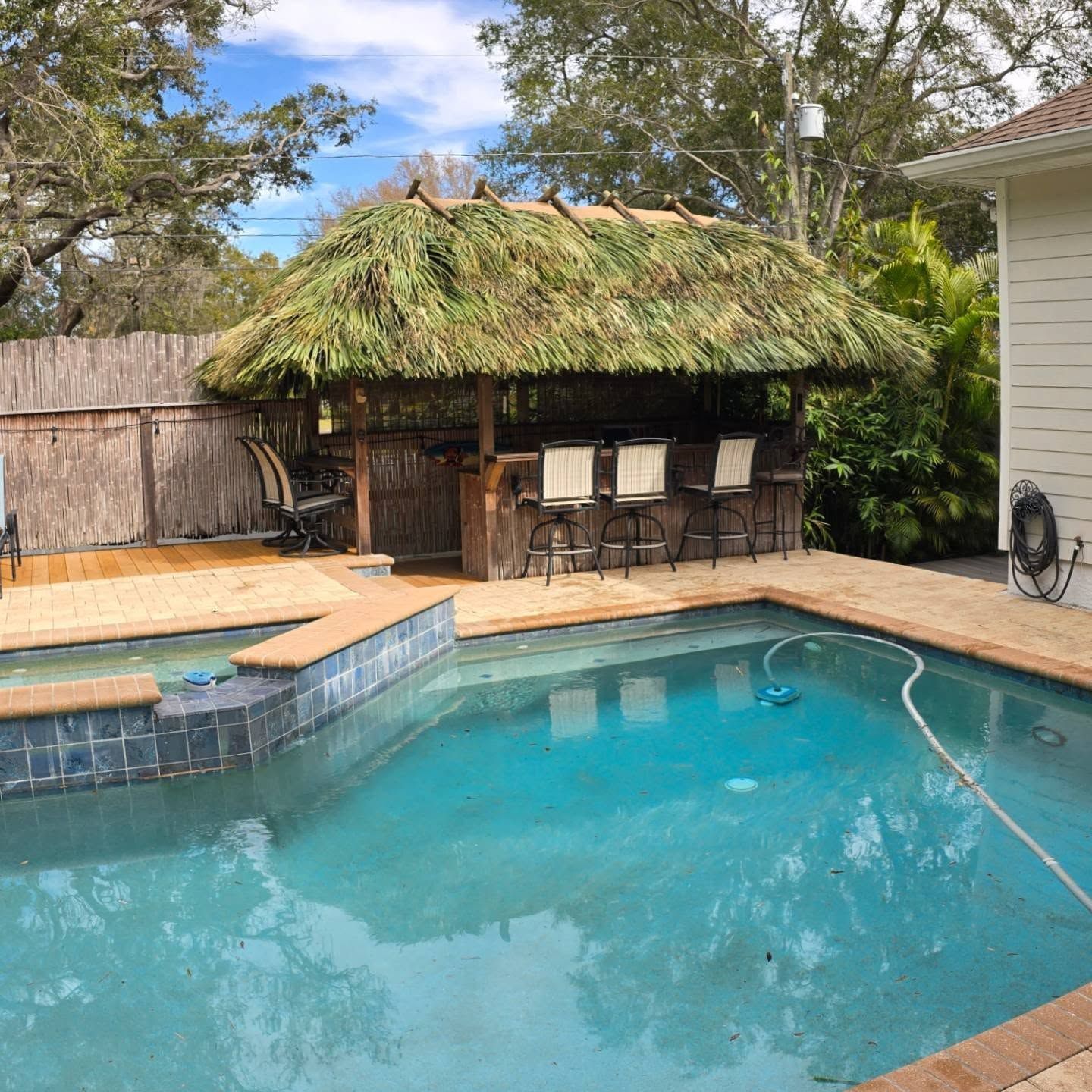 Poolside tiki bar with thatched roof, stools, and pool with blue water.