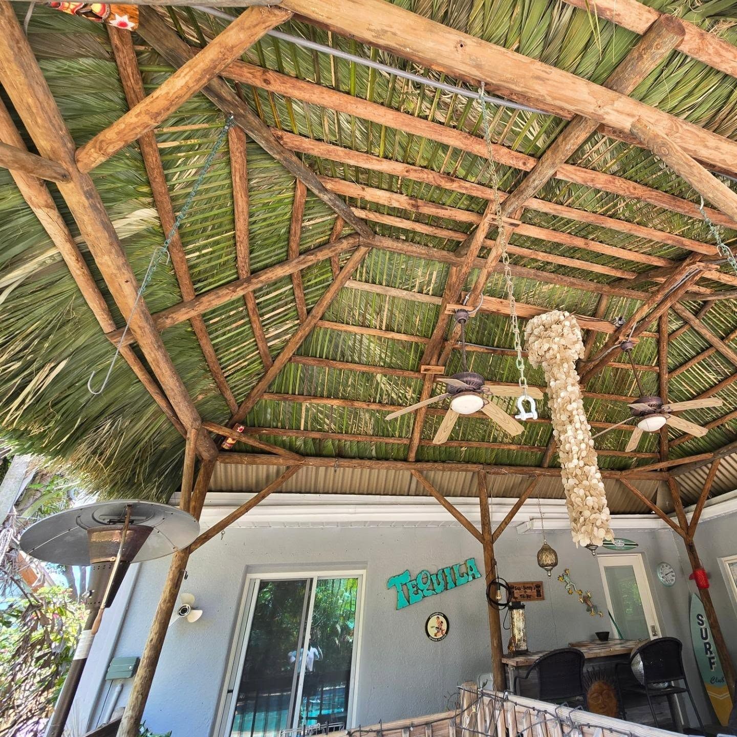 A wooden tiki-style roof covers a patio. Two ceiling fans hang from the structure.