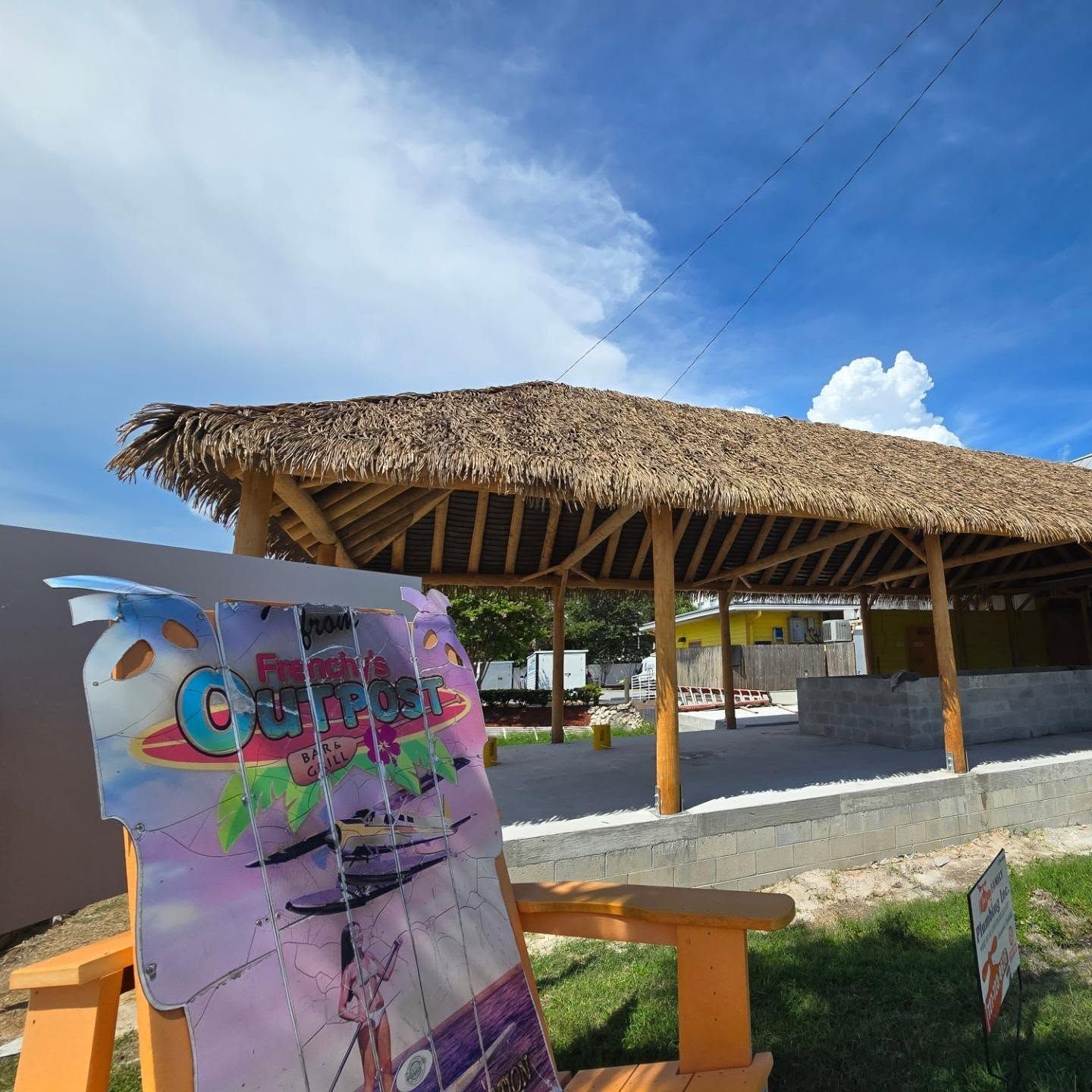 A thatched roof structure with a colorful sign in the foreground under a blue sky.
