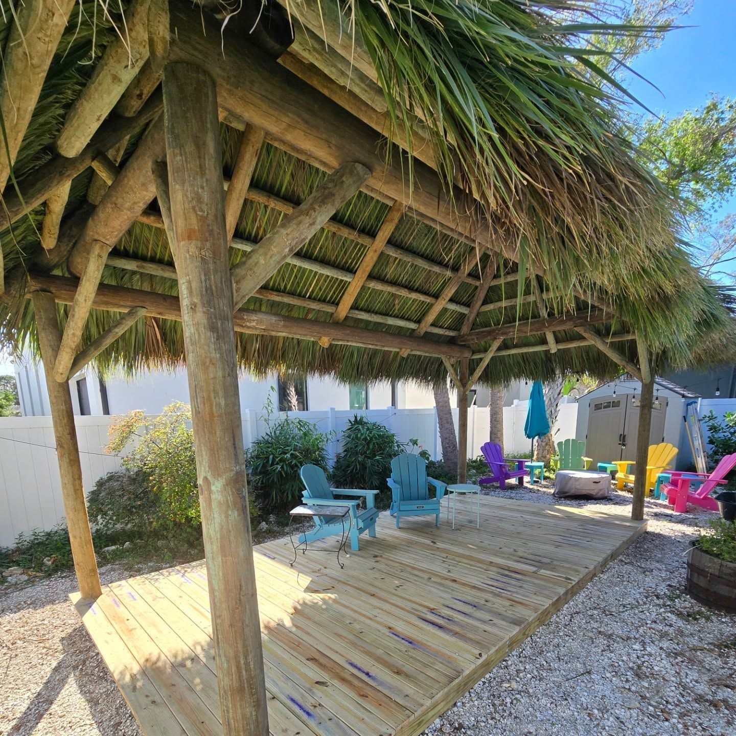 Wooden tiki hut over a deck with colorful Adirondack chairs; bright outdoor setting.