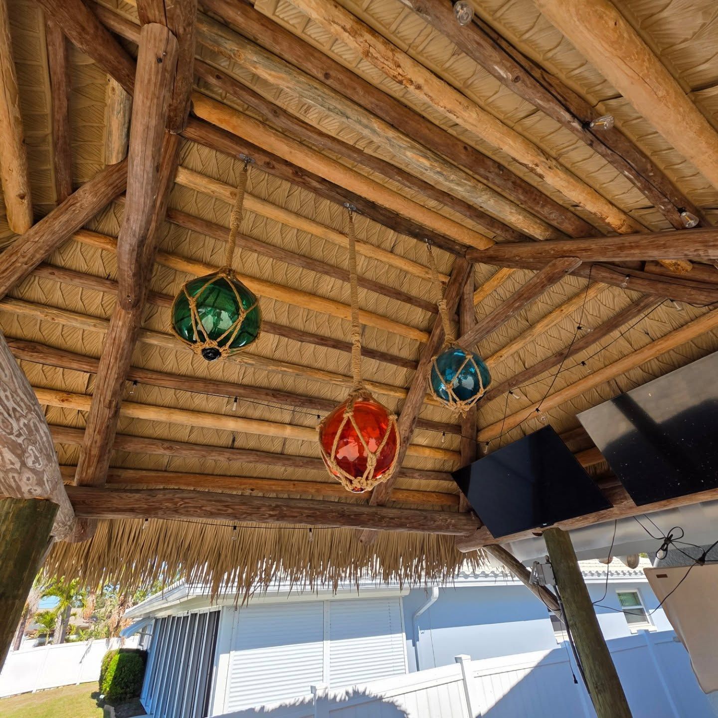 Three colorful hanging glass globes under a thatched roof structure.
