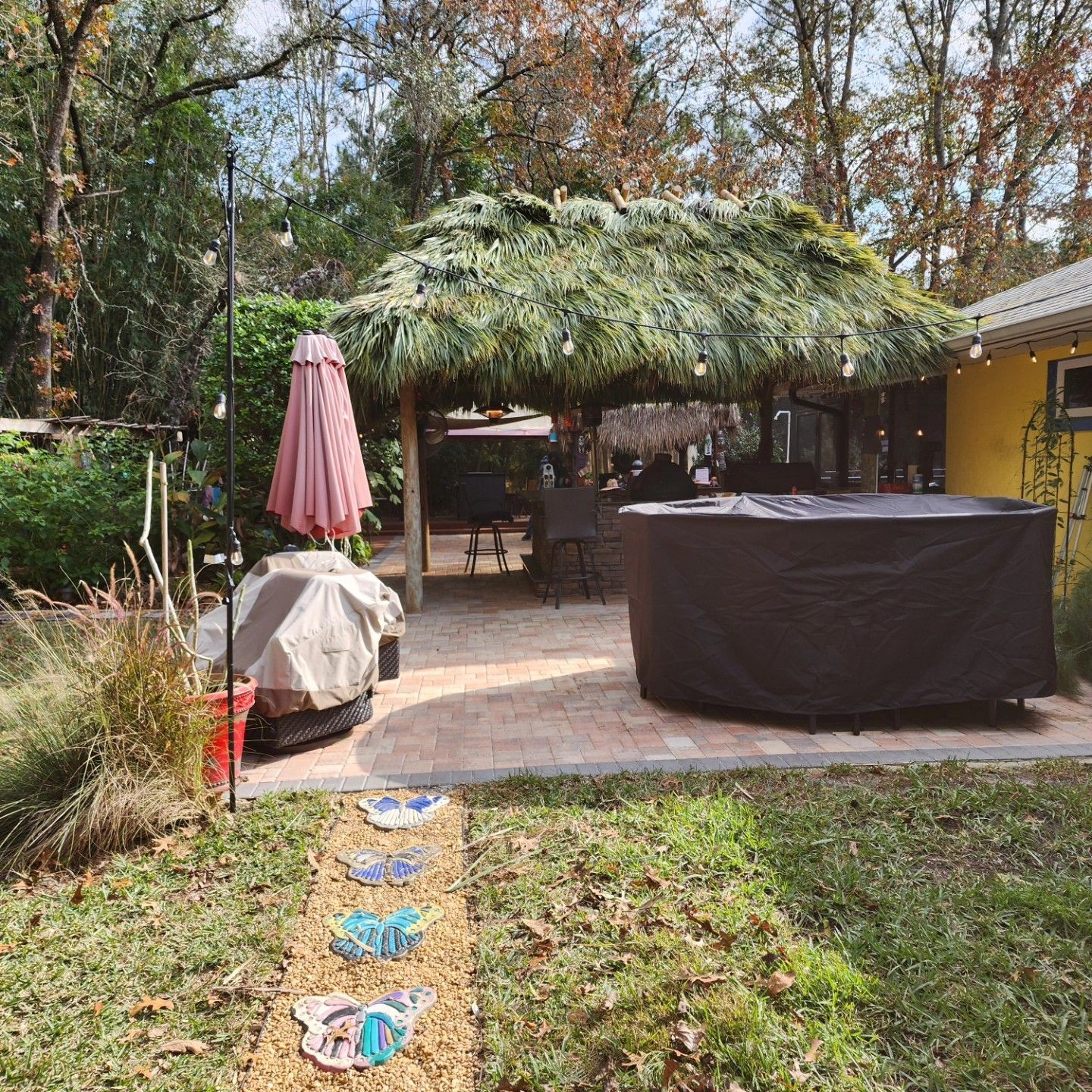 A patio with a thatched roof covering, a hot tub, and a closed umbrella in a backyard.