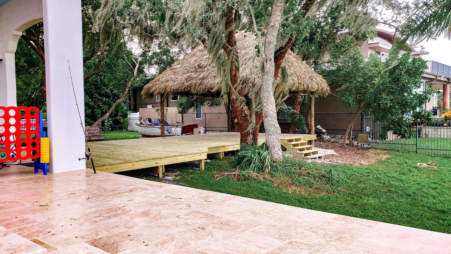 Tiki hut with thatched roof, deck, and Connect Four game in a backyard setting.