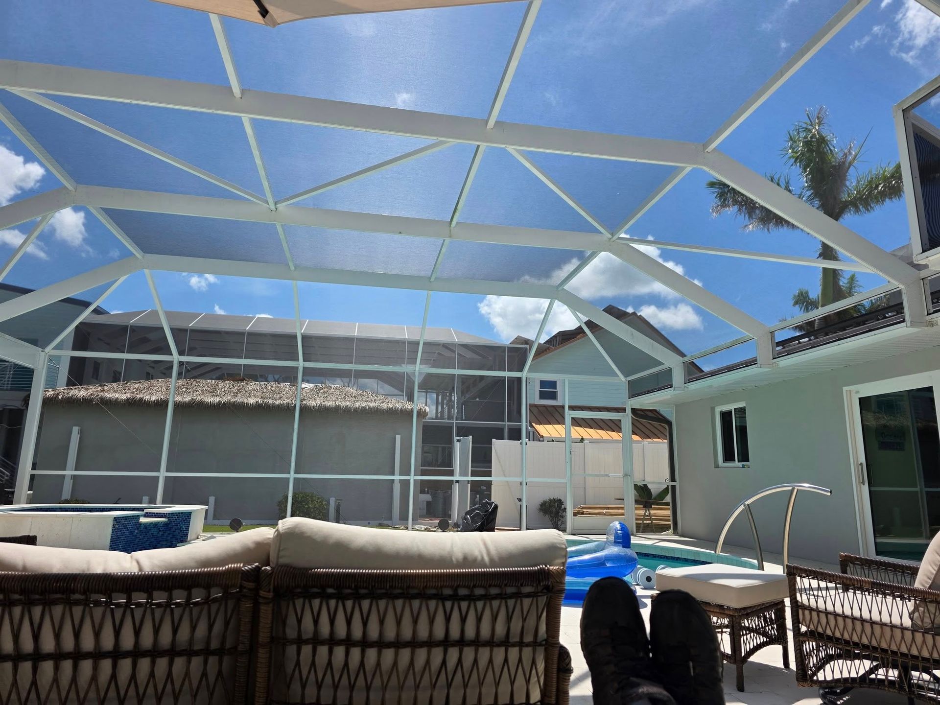 Pool patio with white screened enclosure, wicker furniture, and blue sky.