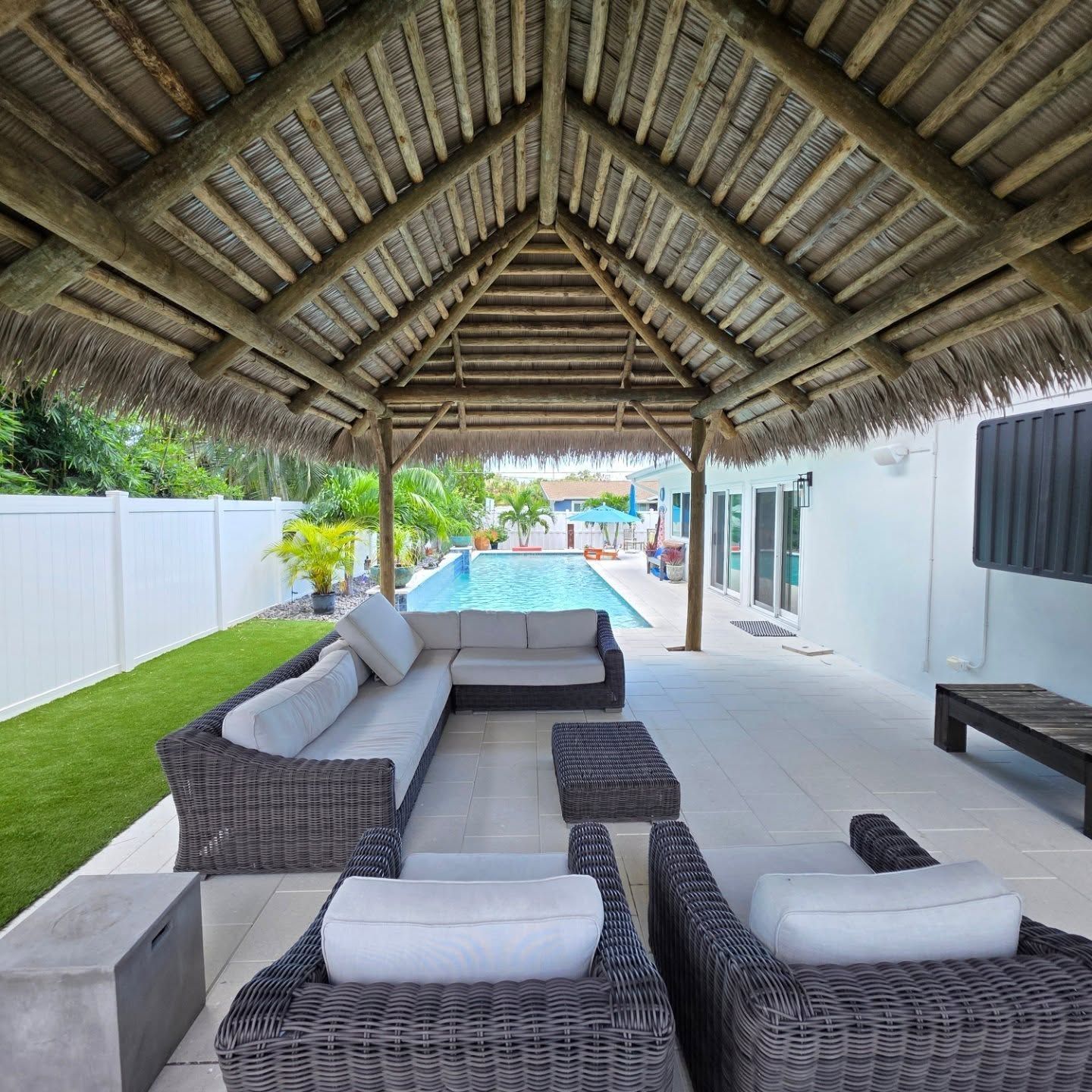 Outdoor seating area under a thatched roof, with a pool visible in the background. Outdoor seating area under a thatched roof, with a pool visible in the background.