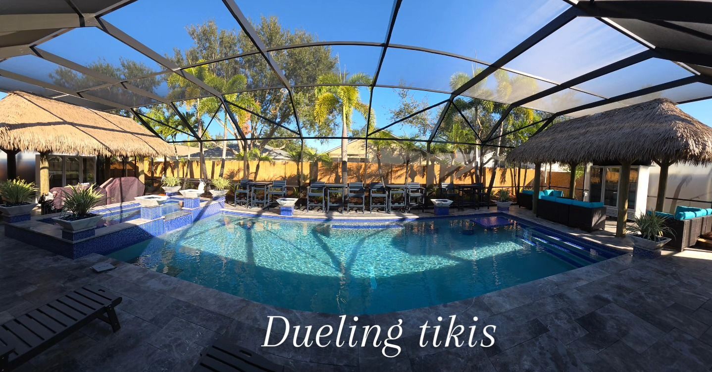 A backyard pool with two tiki huts, surrounded by a screened enclosure under a clear blue sky.