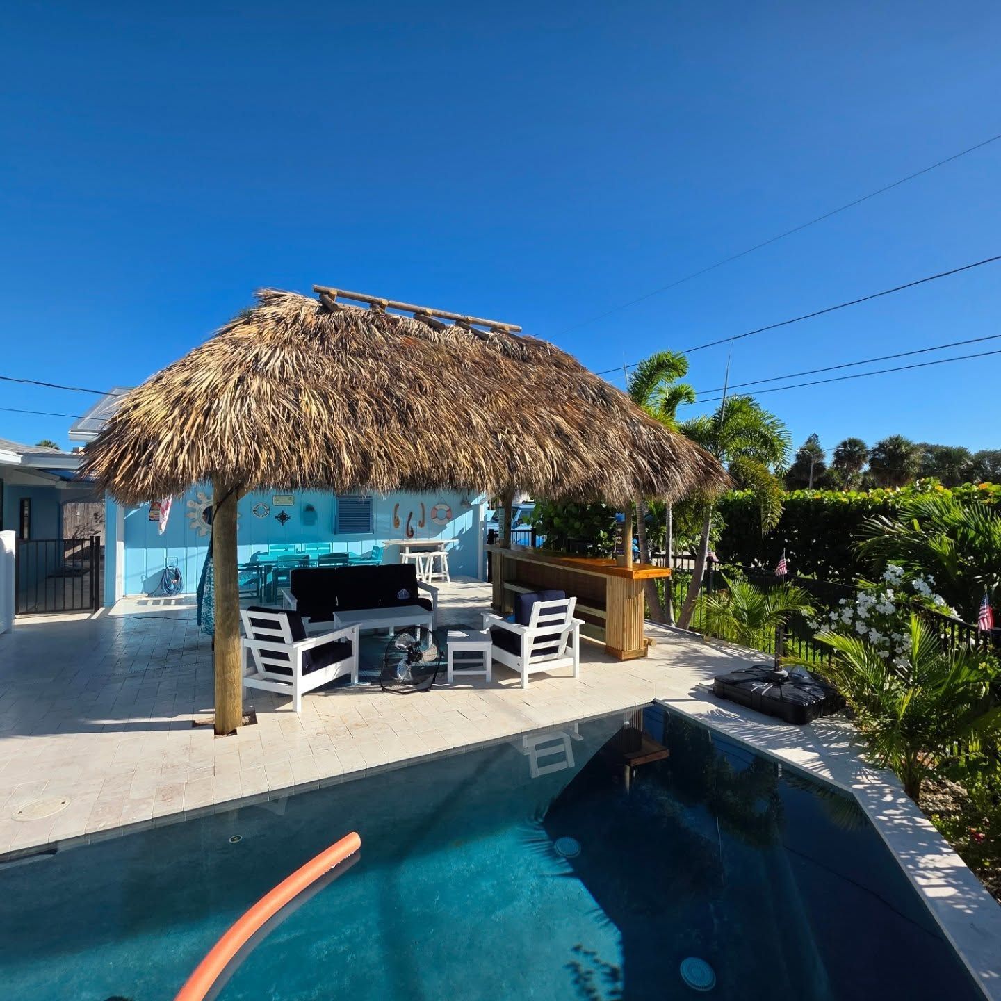 Gazebo with thatched roof, curtains, and cushions on a lawn with stepping stones and lush greenery.