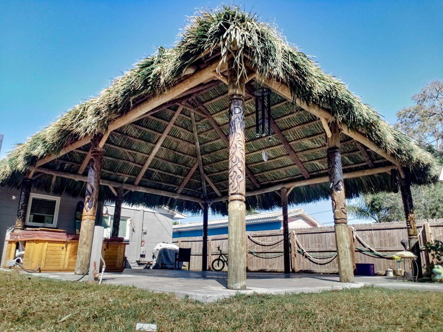Thatched-roof outdoor gazebo with wood posts, on a sunny day.