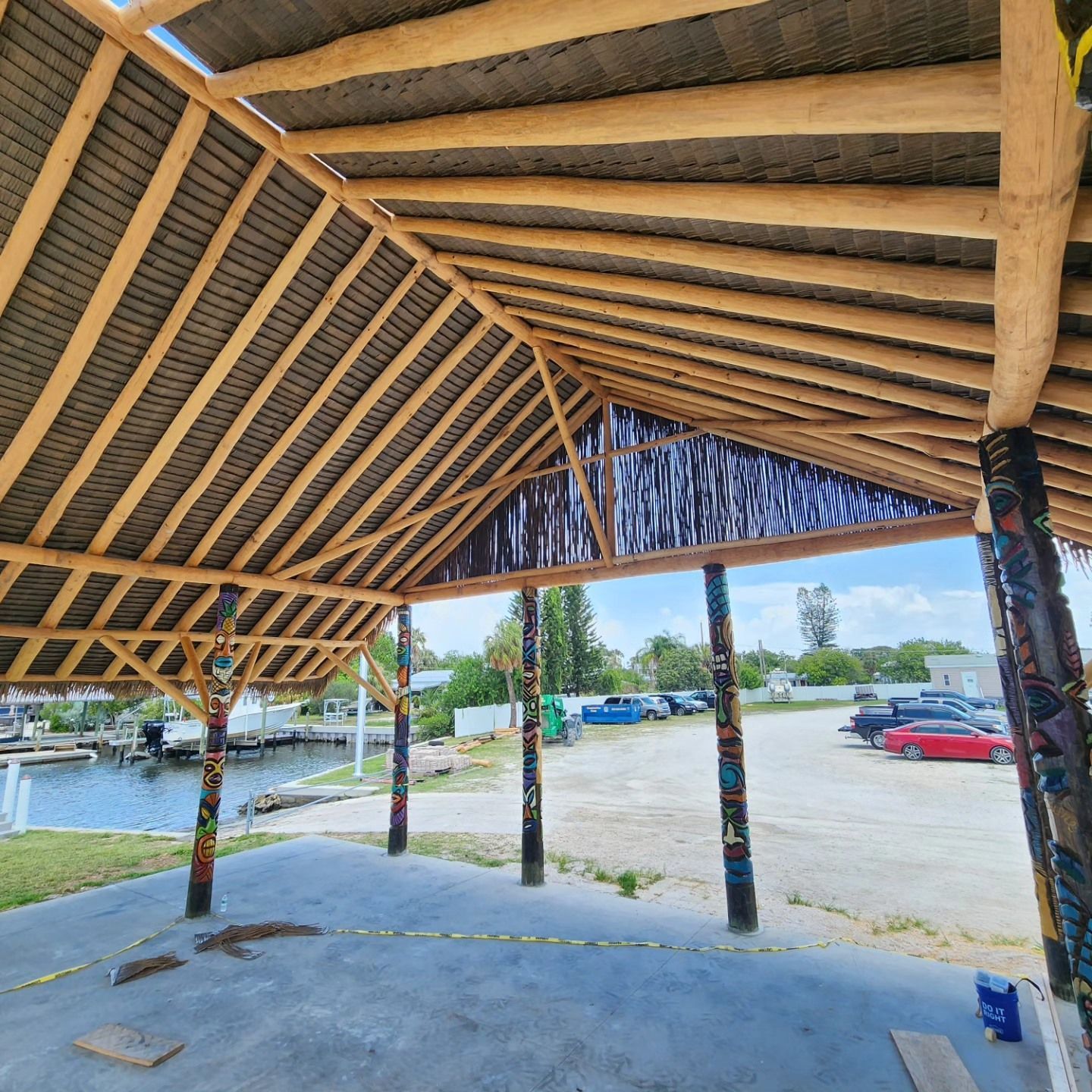 Covered outdoor structure with a view of a waterfront and parking lot. Wooden beams, corrugated roof.