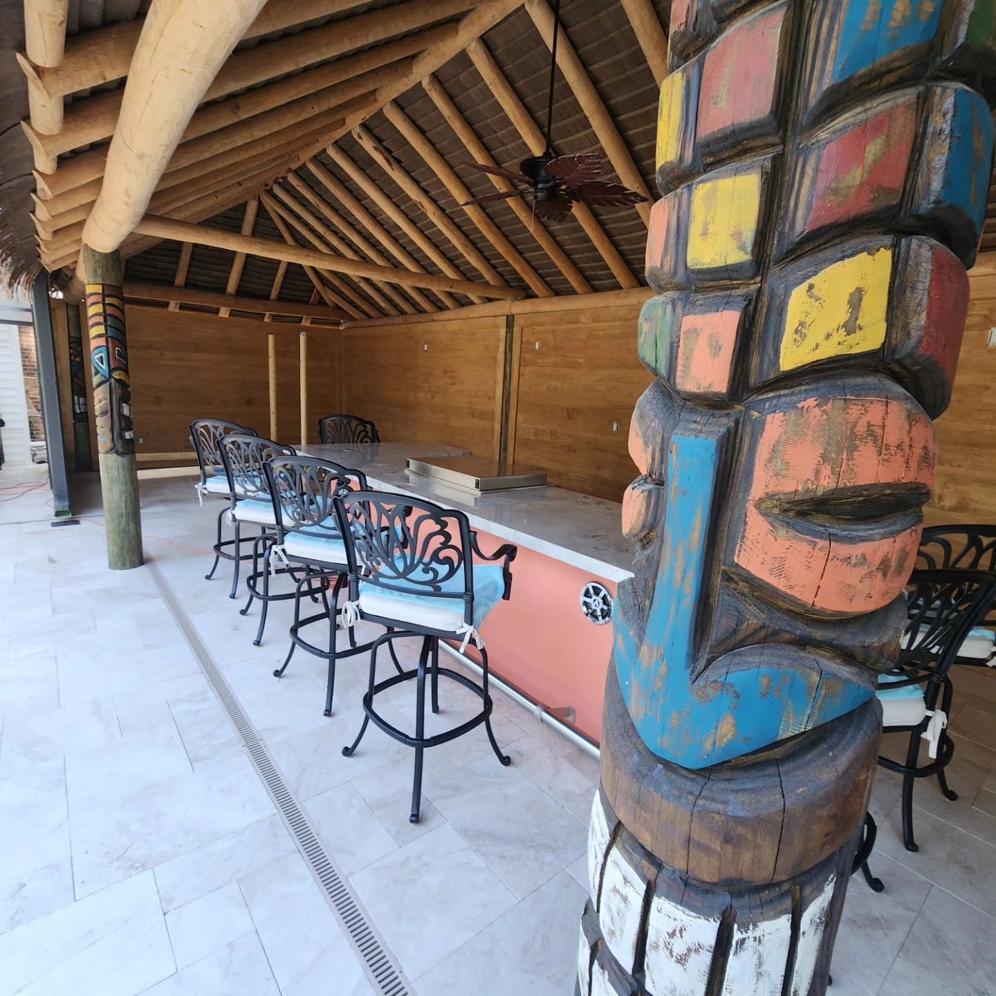 Outdoor tiki bar with carved totem, bar stools, and thatched roof.