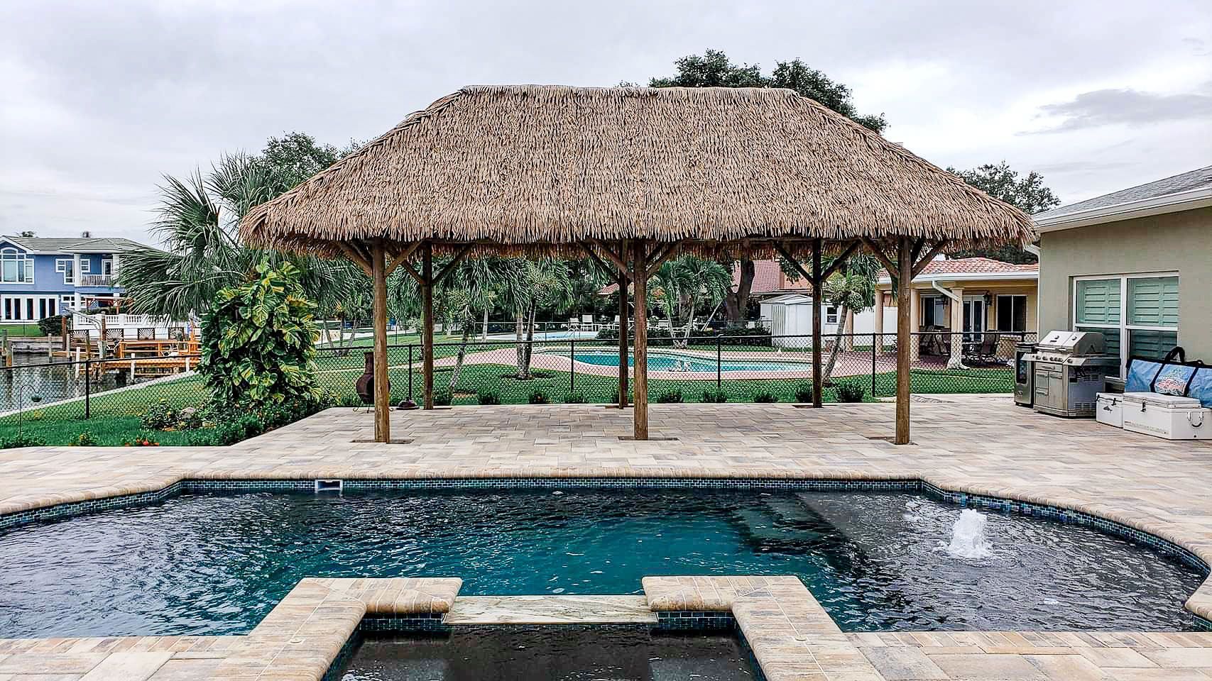 Pool with thatched roof structure; poolside grill, water view in the background.