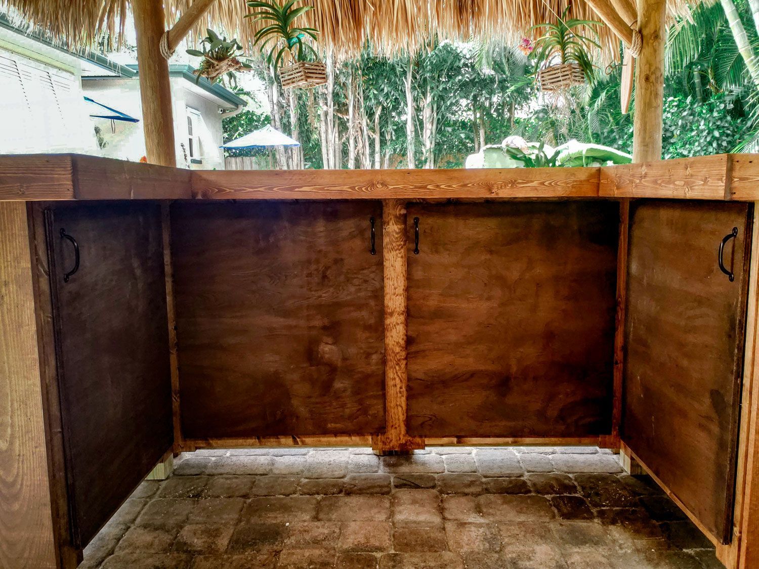 Outdoor bar with wooden counter and doors, under a thatched roof structure.