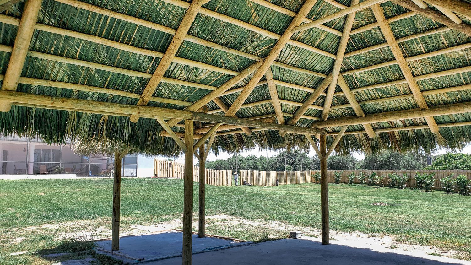 Tiki-style thatched roof structure with wooden beams and posts, set in grassy area.