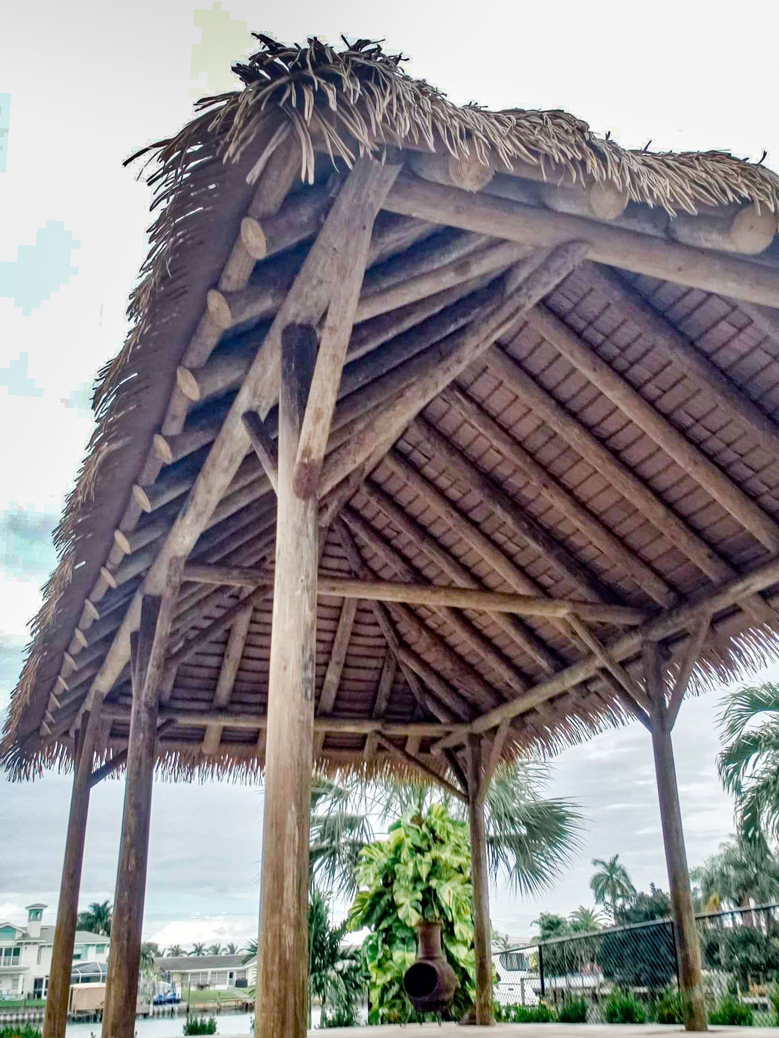 Wooden gazebo with thatched roof, set outdoors. Supporting beams and posts are visible.