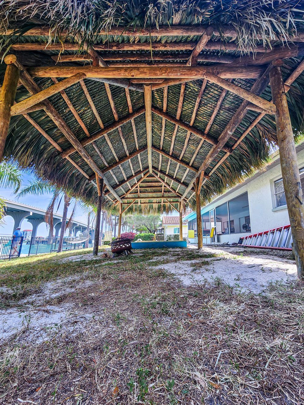 View from inside a thatched roof structure, looking towards a building. Ground is covered in grass.