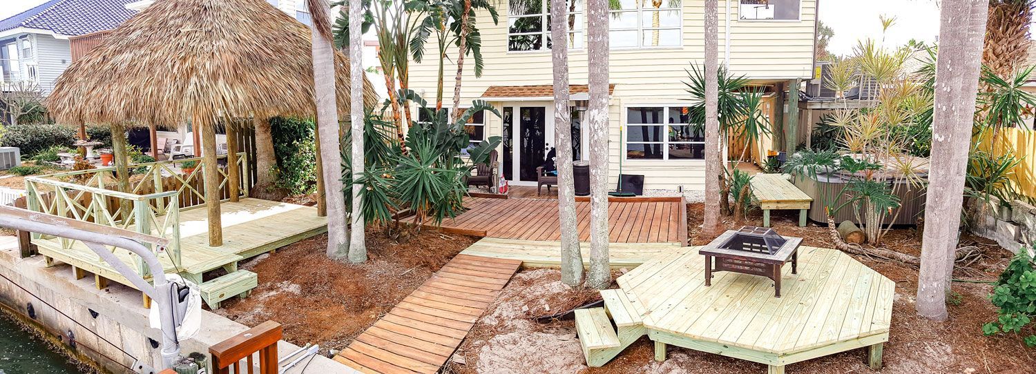 Tropical backyard with tiki hut, dock, fire pit, and deck seating.
