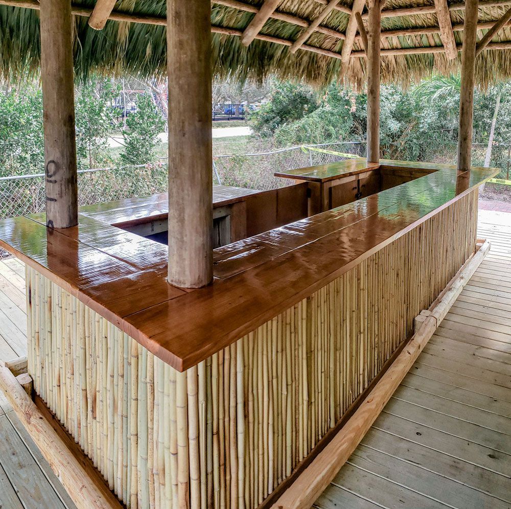 Tiki bar with bamboo siding, a wooden countertop, and a thatched roof, located outdoors.