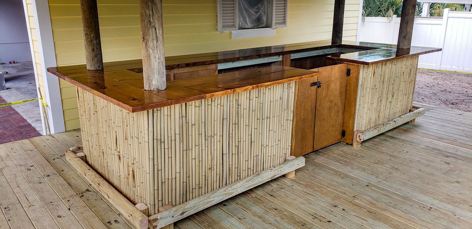Outdoor bar with a bamboo-like exterior, wooden countertop, and supporting posts on a wooden deck.