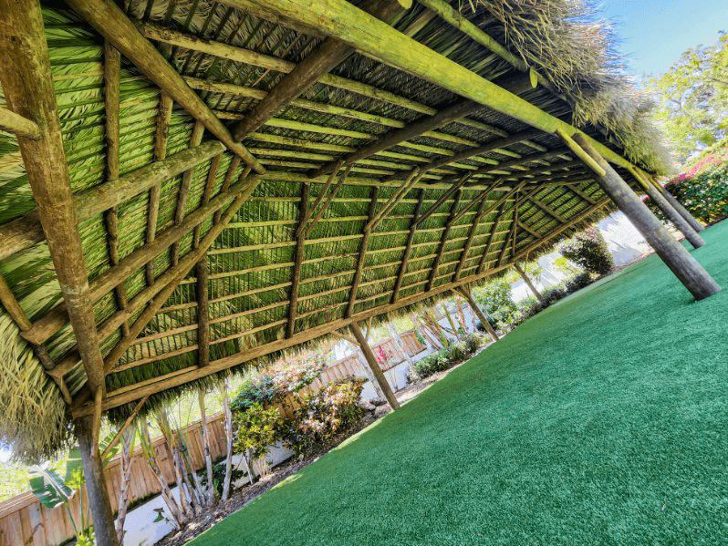 Wooden tiki-style roof with green thatch over artificial turf.