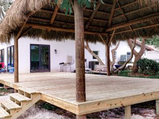 Wooden deck with thatched roof gazebo attached to a white house. Wooden deck with thatched roof gazebo attached to a white house.