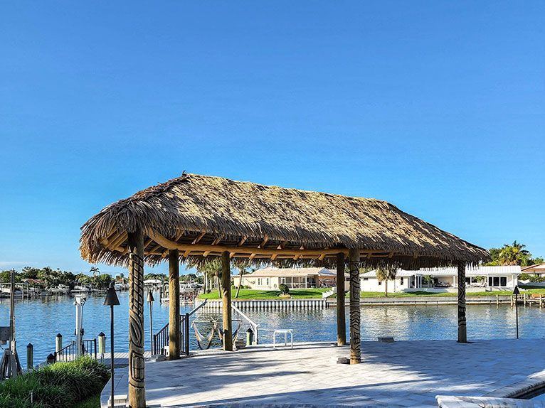 Tiki hut on a dock overlooking water; blue sky, sunny day; residential area in the background. Tiki hut on a dock overlooking water; blue sky, sunny day; residential area in the background.