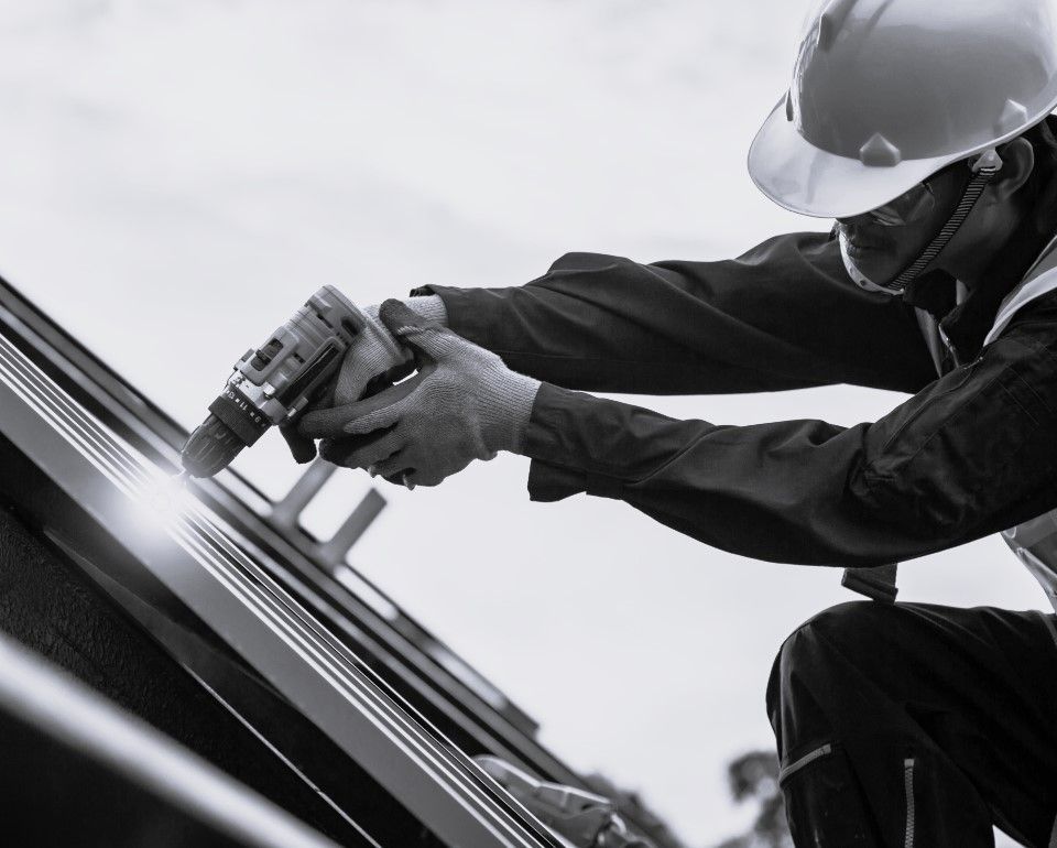 A man wearing a hard hat is working on a roof with a drill.