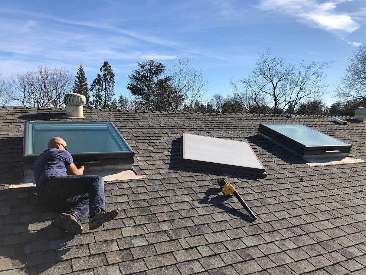 A man is sitting on top of a roof with skylights.
