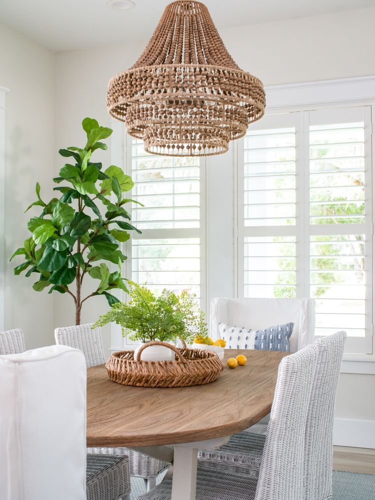 Dining room with wooden table, white chairs, beaded chandelier, and large leafy plant.