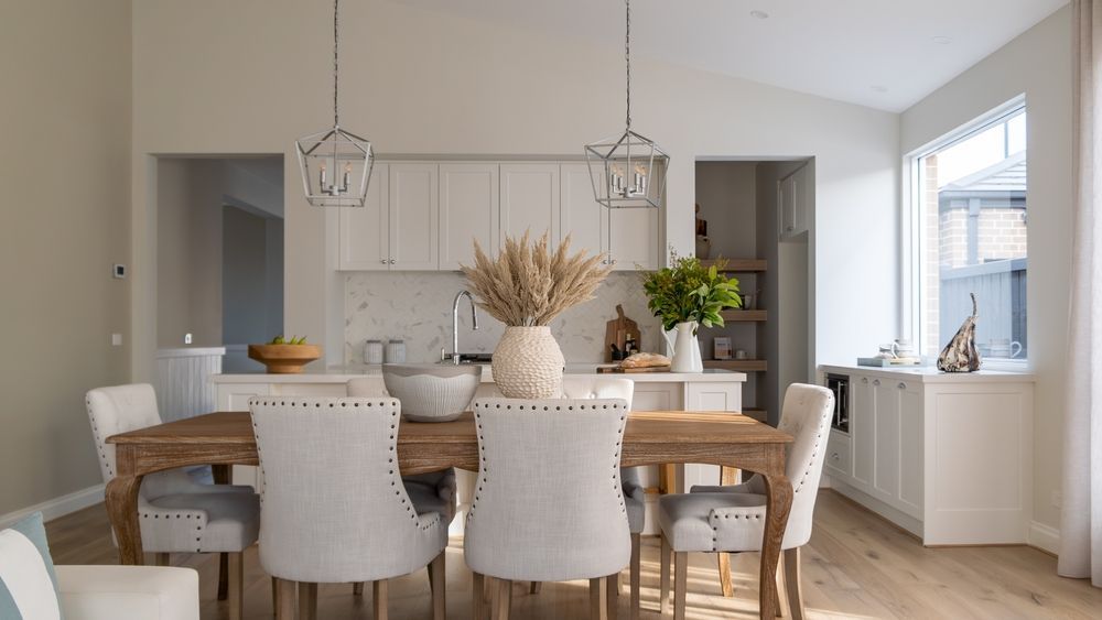 Dining room with wooden table, white chairs, and a kitchen visible in the background.