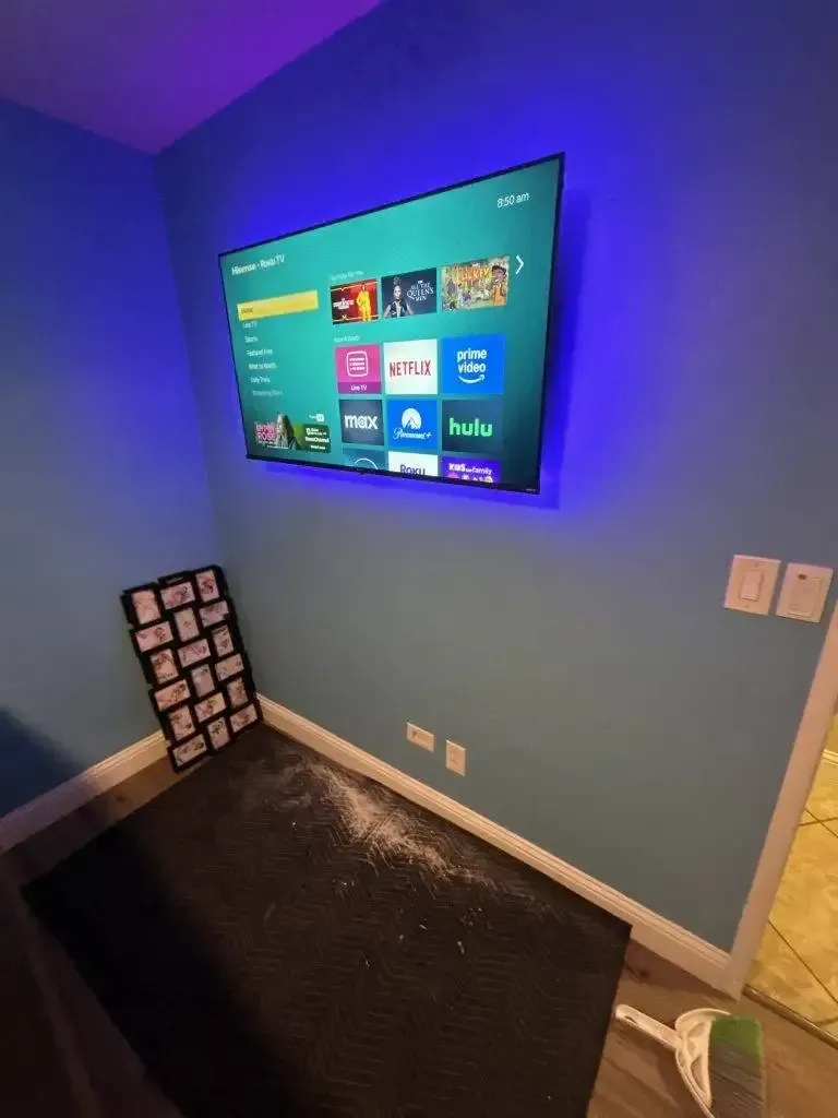A blue-walled room with a wall-mounted TV glowing with blue LED backlighting above a pile of white debris on the carpet.