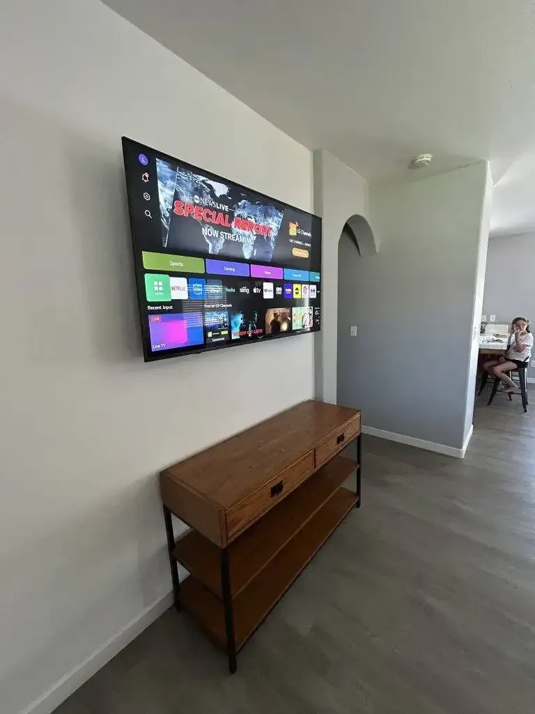 A television mounted on a white wall above a wooden console table in a minimalist living room.