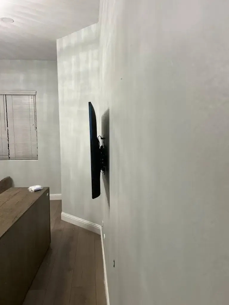 A side view of a flat-screen television mounted on a curved white wall in a room with wood flooring.