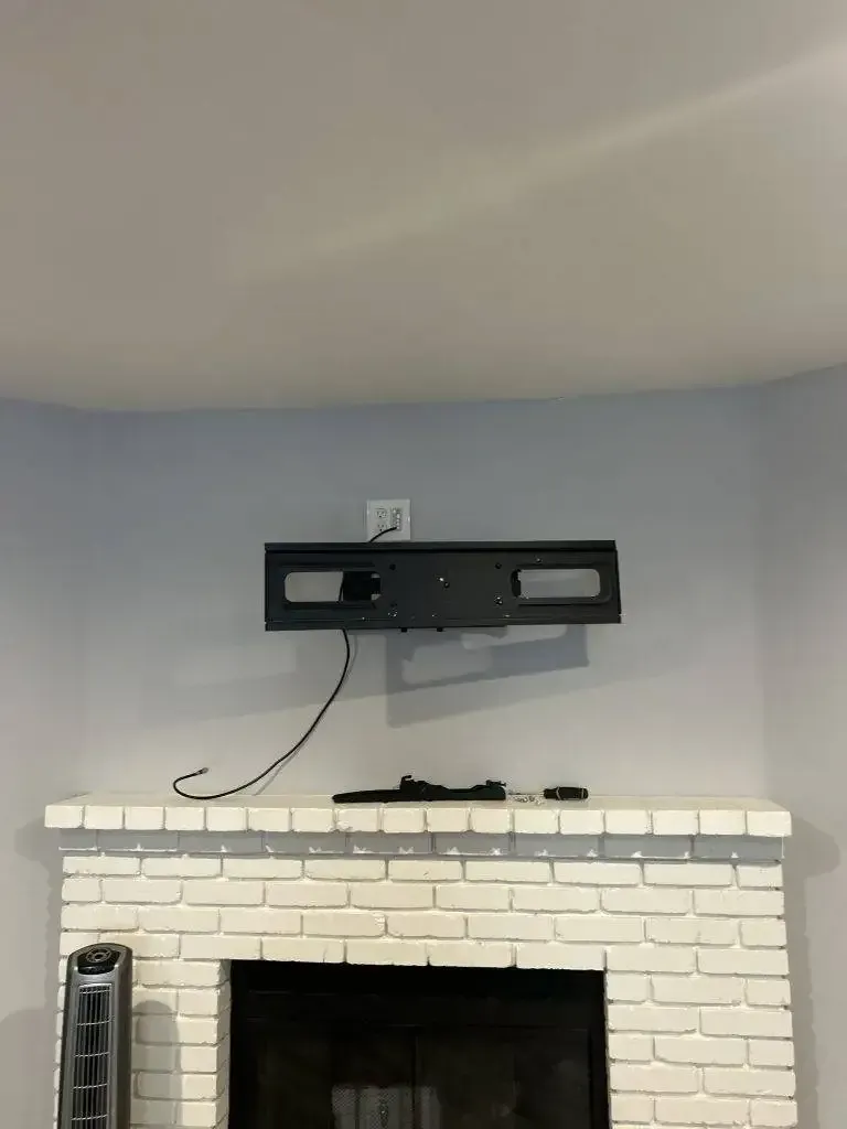 A black TV wall mount is installed on a light blue wall above a painted white brick fireplace.