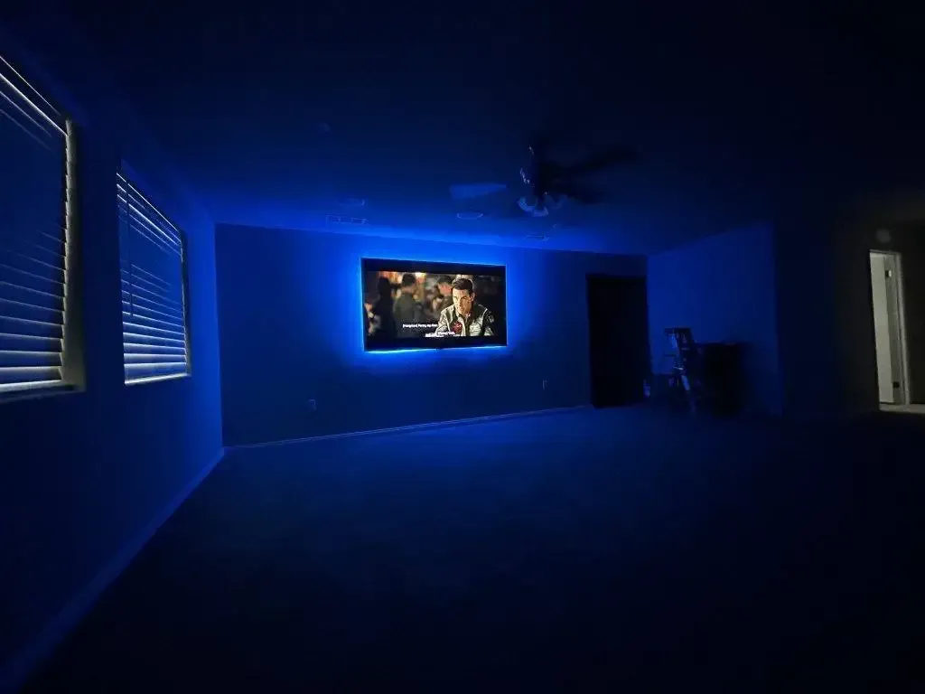 A dimly lit room with a wall-mounted television glowing with blue LED backlighting, creating a cinematic atmosphere.