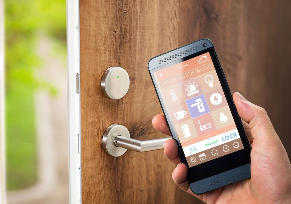 A hand holds a smartphone displaying a home automation app, ready to unlock a wooden door with a modern handle.